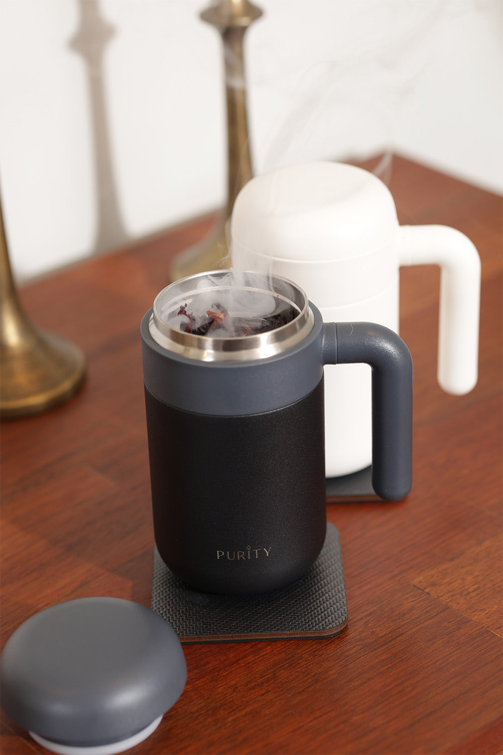 Infuso Essence en color negro sobre una mesa. El infusor está destapado y en su interior hay té humeante.