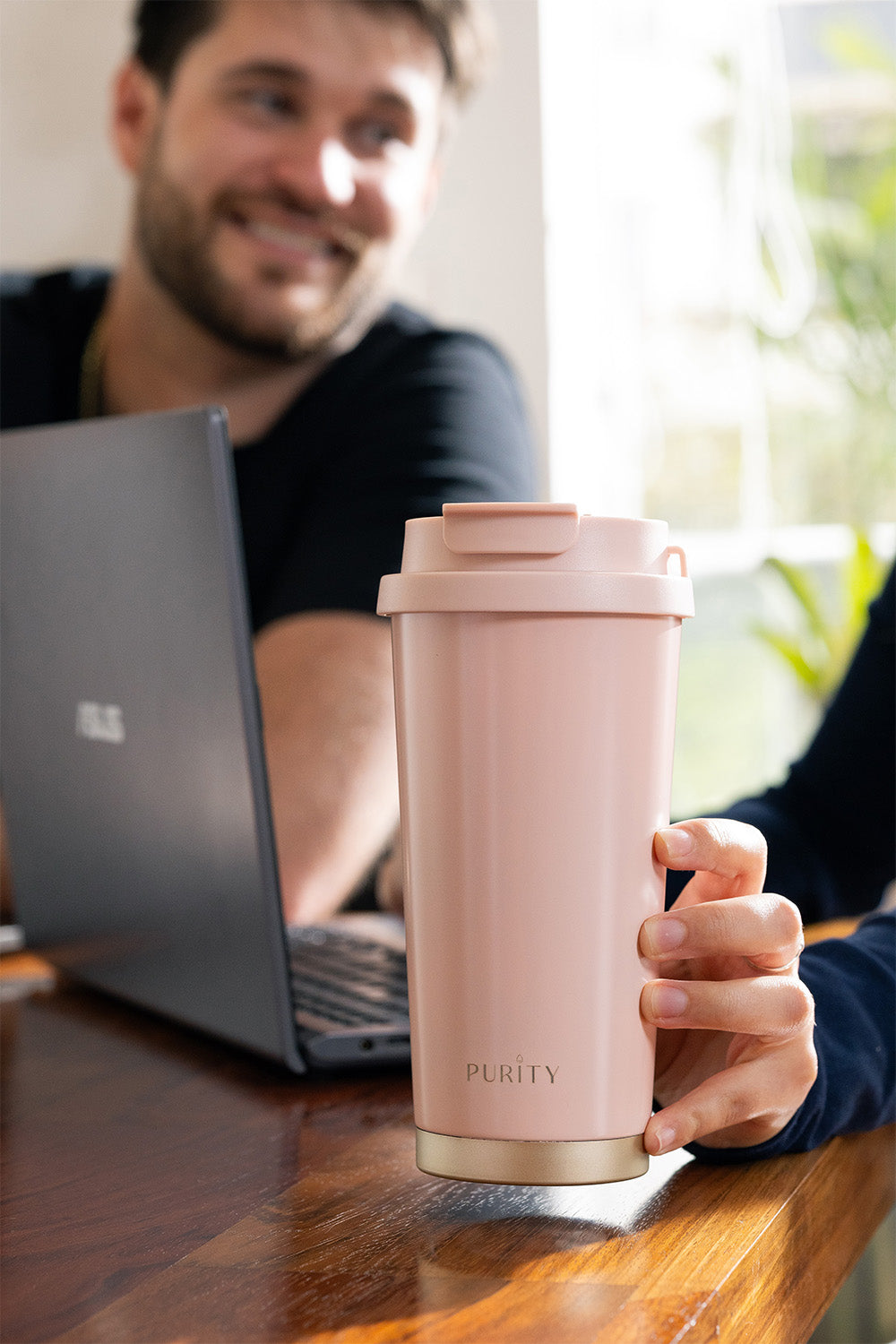 Taza de café Deluxe color rosado sobre un escritorio. Una mano lo sostiene.