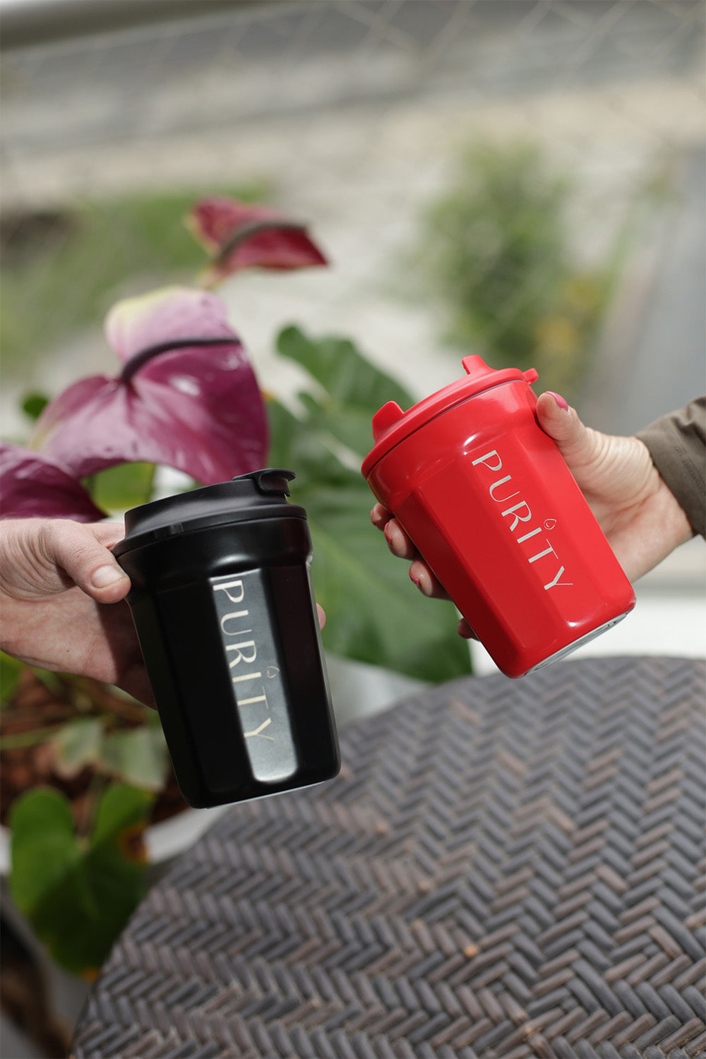 Dos manos sostienen cada una una taza ceramic cup. Una es color rojo y la otra negro.